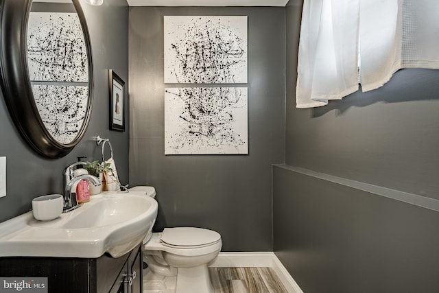 half bath featuring vanity, toilet, wood finished floors, and baseboards