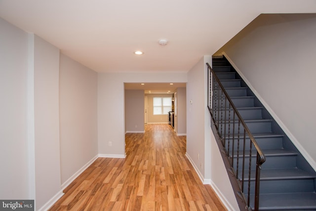 hallway featuring light wood finished floors, stairway, recessed lighting, and baseboards