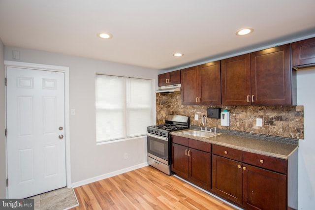 kitchen featuring under cabinet range hood, a sink, decorative backsplash, stainless steel gas stove, and light wood finished floors