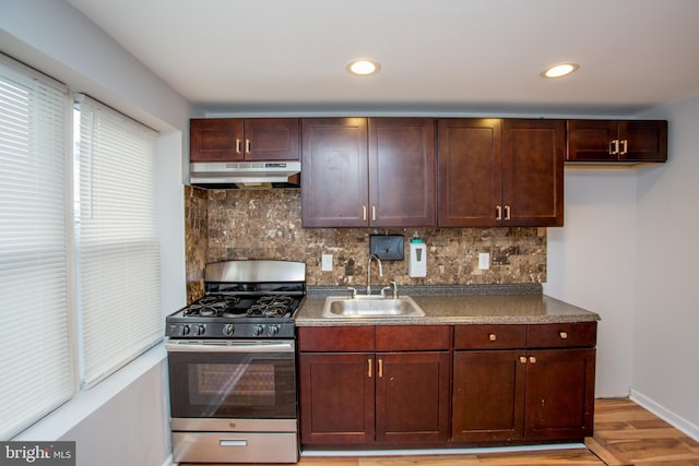 kitchen featuring light wood finished floors, tasteful backsplash, stainless steel gas range, under cabinet range hood, and a sink