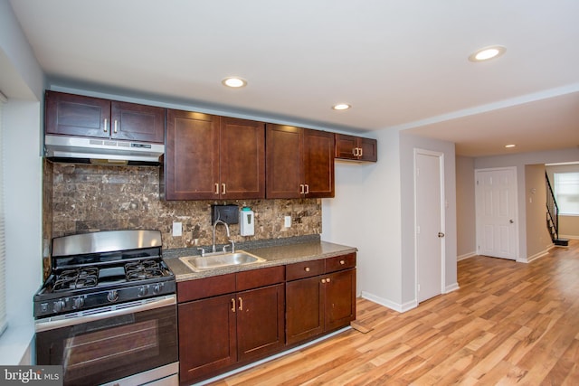 kitchen with light wood-style flooring, under cabinet range hood, a sink, decorative backsplash, and gas stove