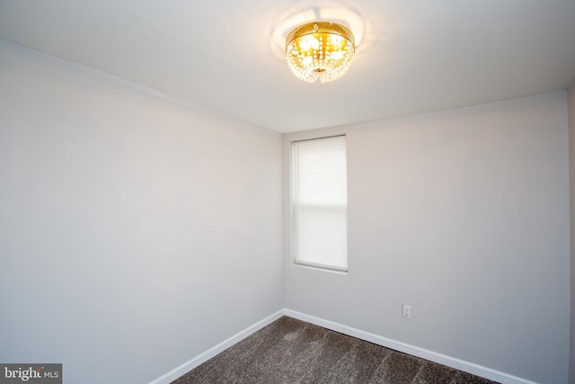 unfurnished room with a chandelier, dark carpet, and baseboards