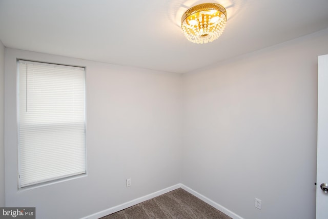 unfurnished room featuring dark colored carpet, baseboards, and an inviting chandelier