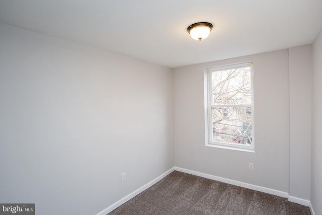 spare room with dark carpet and baseboards