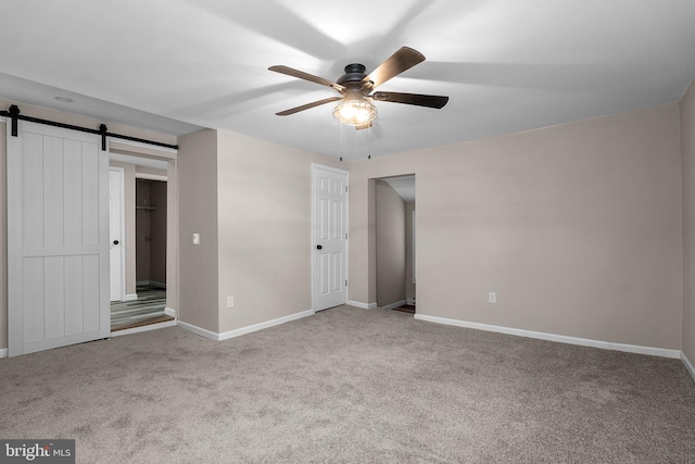 unfurnished bedroom featuring a ceiling fan, carpet flooring, baseboards, and a barn door