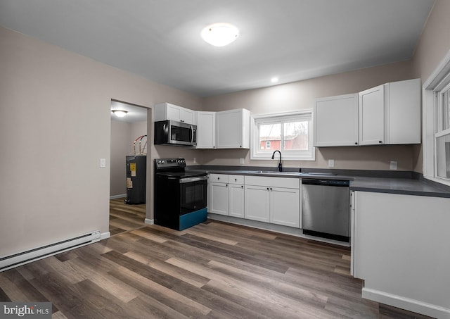 kitchen with dark countertops, a baseboard radiator, appliances with stainless steel finishes, white cabinetry, and a sink