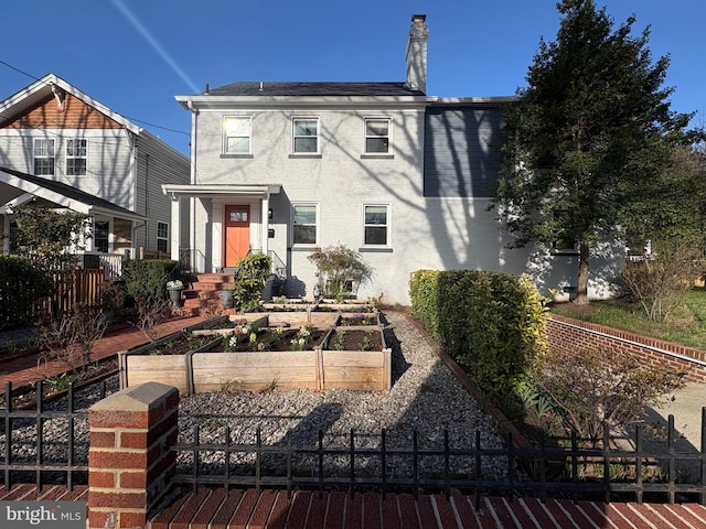 view of front of house with a garden, fence, a chimney, brick siding, and a shingled roof