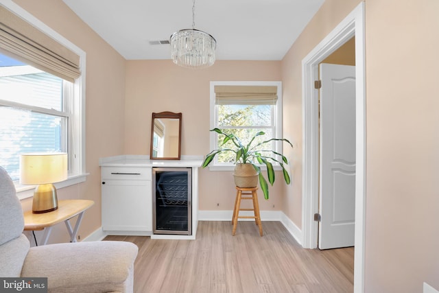 living area with light wood-style flooring, visible vents, a chandelier, baseboards, and beverage cooler