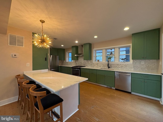 kitchen featuring green cabinetry, a sink, wall chimney exhaust hood, stainless steel appliances, and visible vents