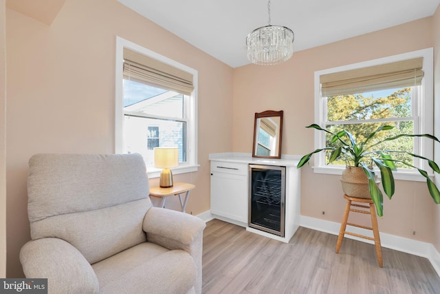 living area with baseboards, light wood finished floors, a chandelier, and beverage cooler