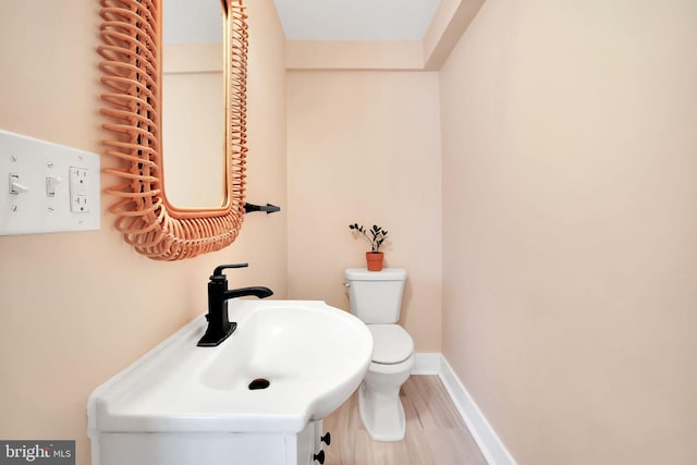 half bath with baseboards, a sink, toilet, and wood finished floors