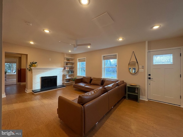 living room featuring a fireplace with raised hearth, a ceiling fan, light wood-type flooring, and plenty of natural light