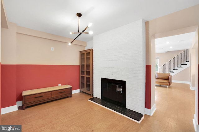 living room featuring baseboards, a fireplace, wood finished floors, stairway, and an inviting chandelier