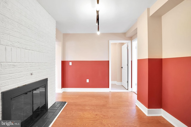 unfurnished living room with baseboards, light wood-type flooring, and a brick fireplace