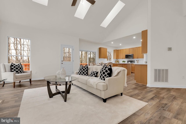 living room featuring visible vents, high vaulted ceiling, a skylight, and light wood-style flooring