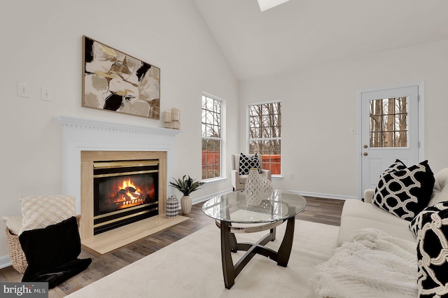 living area with baseboards, a fireplace with flush hearth, high vaulted ceiling, and wood finished floors