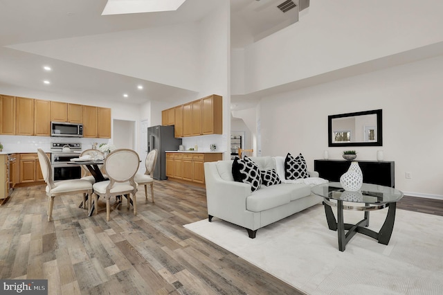 living area featuring baseboards, visible vents, high vaulted ceiling, light wood-style flooring, and recessed lighting