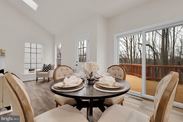 dining space featuring a skylight, visible vents, high vaulted ceiling, and wood finished floors