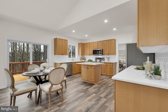 kitchen featuring lofted ceiling, light wood-style flooring, light countertops, appliances with stainless steel finishes, and a center island