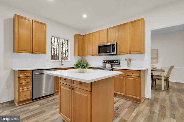 kitchen with a sink, light countertops, appliances with stainless steel finishes, light wood-type flooring, and a center island