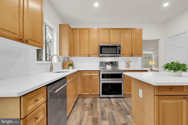 kitchen featuring tasteful backsplash, light countertops, light wood-style floors, stainless steel appliances, and a sink