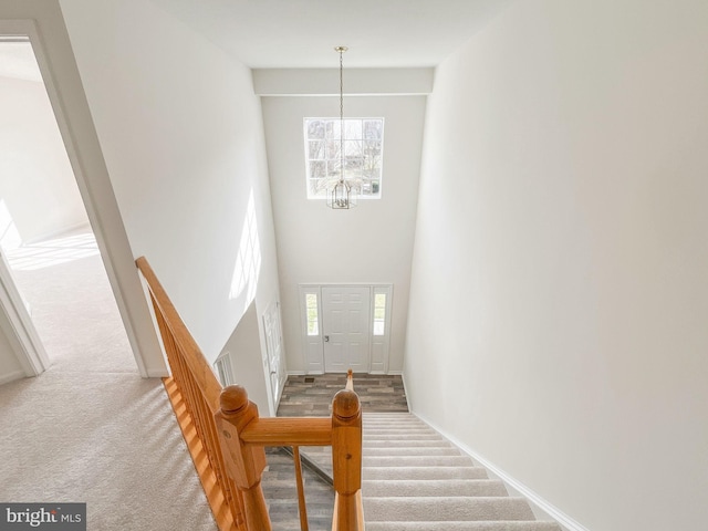 carpeted entrance foyer featuring an inviting chandelier, a high ceiling, and baseboards