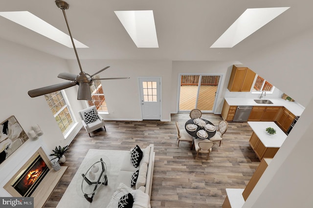 living room with a glass covered fireplace, wood finished floors, vaulted ceiling with skylight, baseboards, and ceiling fan