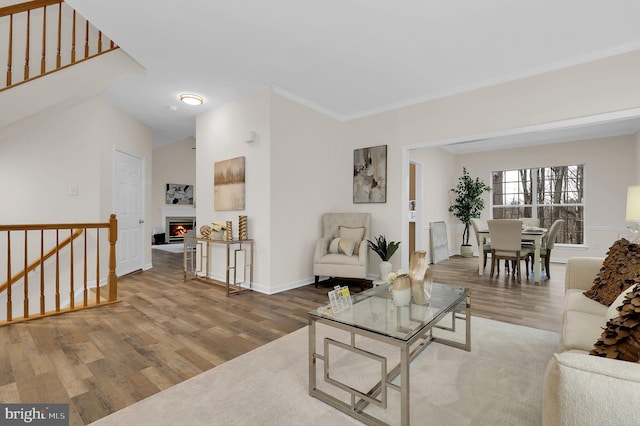 living area featuring ornamental molding, wood finished floors, a lit fireplace, baseboards, and stairs