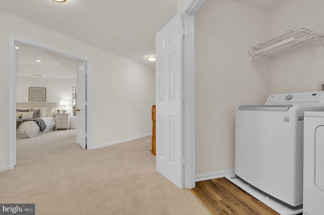 clothes washing area with laundry area, washing machine and dryer, light colored carpet, and baseboards