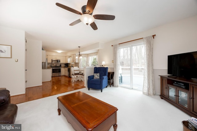 living area with ceiling fan with notable chandelier and light wood-type flooring