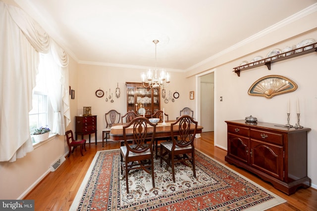 dining area featuring light wood-type flooring, a notable chandelier, visible vents, and crown molding