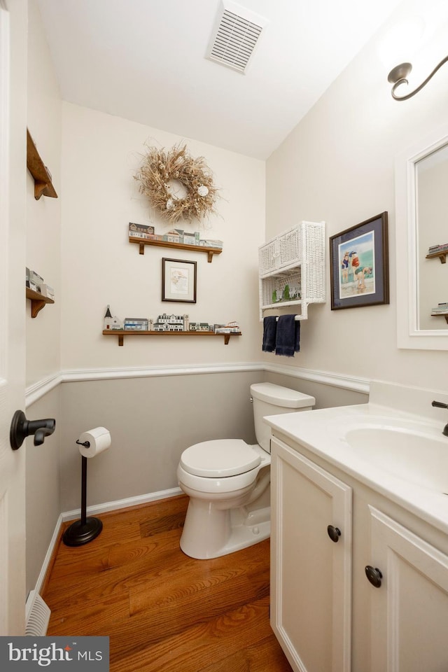 half bath featuring visible vents, toilet, wood finished floors, baseboards, and vanity