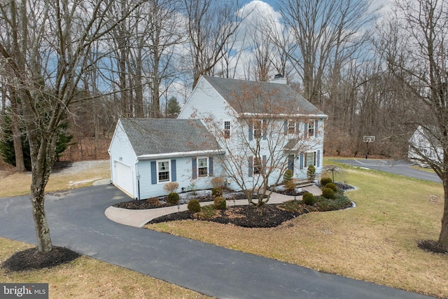 colonial home featuring a front lawn, aphalt driveway, a shingled roof, a garage, and a chimney