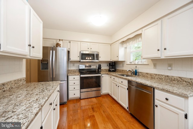 kitchen with tasteful backsplash, light wood-type flooring, appliances with stainless steel finishes, white cabinets, and a sink