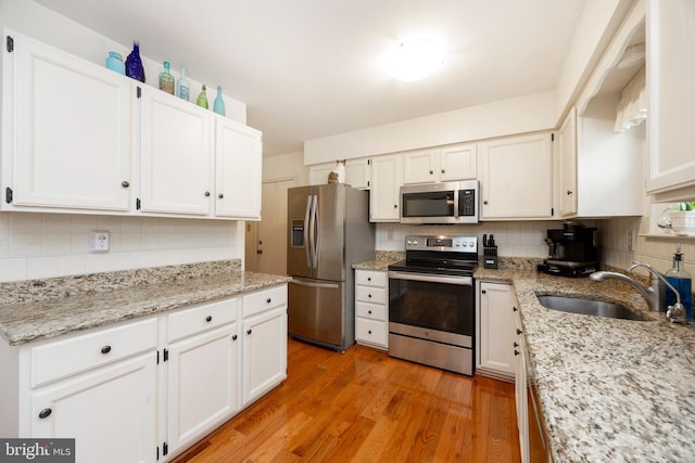 kitchen featuring decorative backsplash, light wood-style flooring, appliances with stainless steel finishes, white cabinetry, and a sink