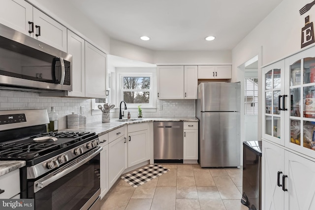 kitchen with light tile patterned flooring, a sink, appliances with stainless steel finishes, backsplash, and light stone countertops