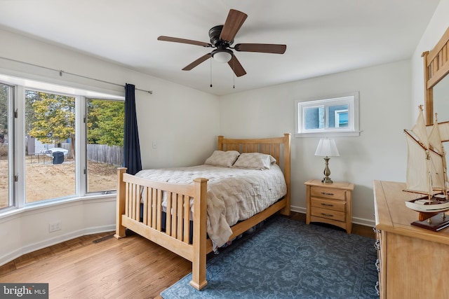 bedroom featuring ceiling fan, multiple windows, wood finished floors, and baseboards