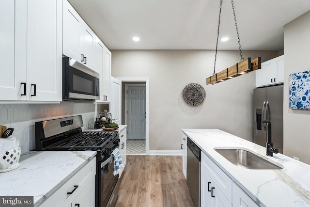 kitchen featuring wood finished floors, a sink, stainless steel appliances, white cabinetry, and backsplash