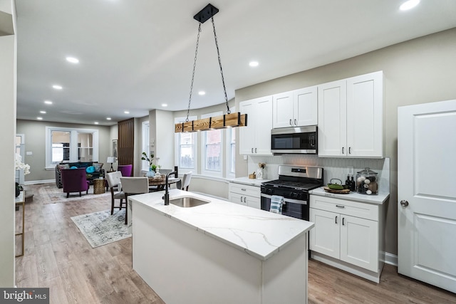 kitchen with appliances with stainless steel finishes, hanging light fixtures, a sink, and light wood-style flooring