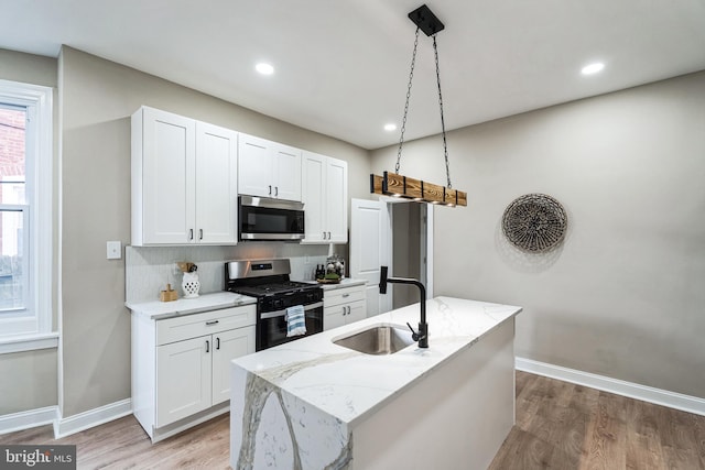 kitchen with light wood finished floors, appliances with stainless steel finishes, white cabinets, and a sink