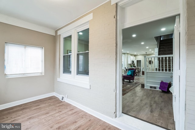 interior space featuring brick wall, ornamental molding, wood finished floors, and baseboards