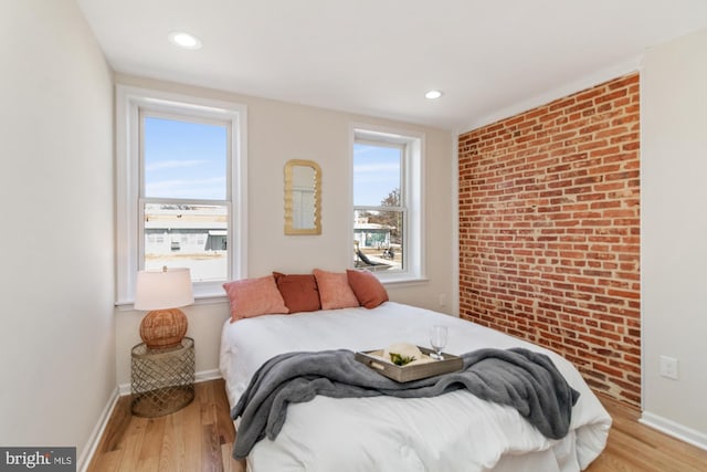 bedroom with multiple windows, brick wall, and wood finished floors