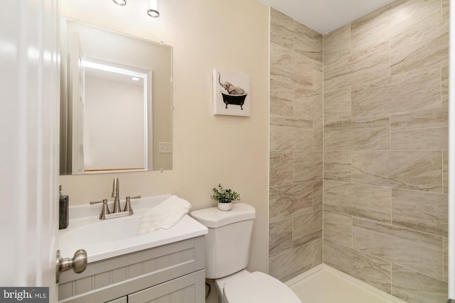 full bath with a tile shower, toilet, and vanity