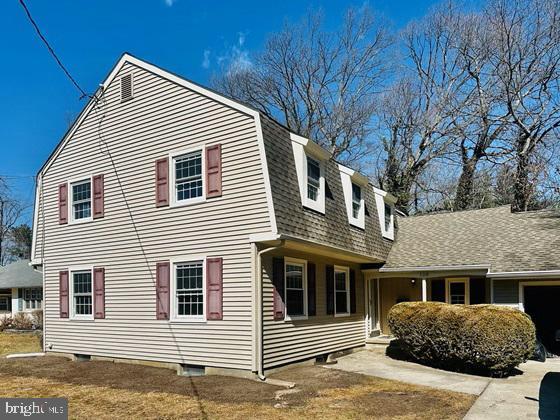 view of side of property featuring a gambrel roof, an attached garage, roof with shingles, and driveway