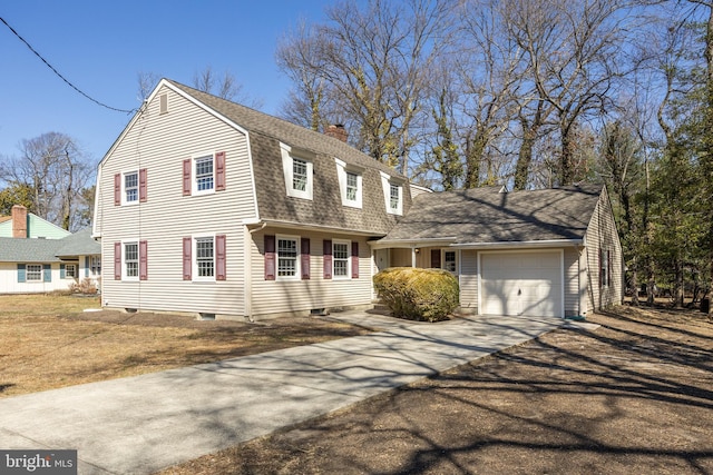 colonial inspired home featuring a gambrel roof, roof with shingles, concrete driveway, an attached garage, and a chimney