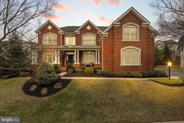 view of front of house with covered porch, a lawn, and brick siding