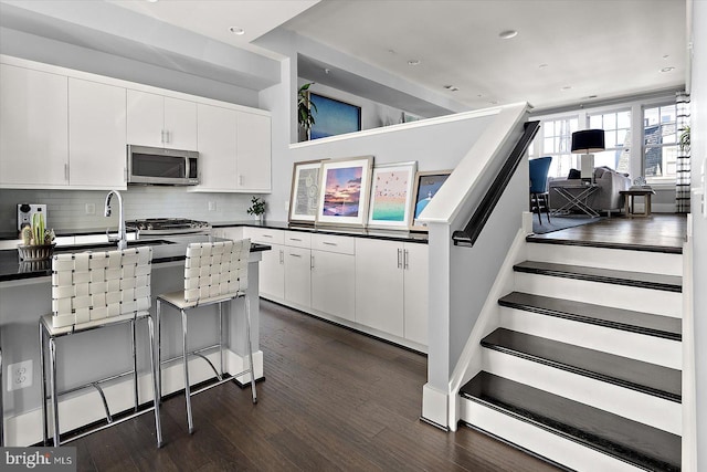 kitchen with dark wood-style flooring, stainless steel microwave, decorative backsplash, and white cabinetry