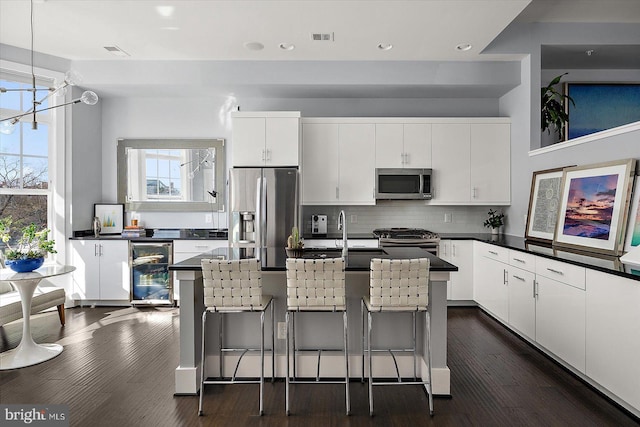 kitchen with appliances with stainless steel finishes, wine cooler, dark countertops, and white cabinetry