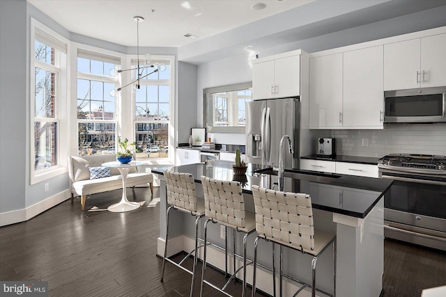 kitchen featuring decorative backsplash, dark countertops, dark wood-style floors, stainless steel appliances, and a sink