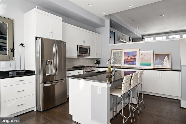 kitchen with a breakfast bar area, dark wood-style flooring, appliances with stainless steel finishes, tasteful backsplash, and dark countertops